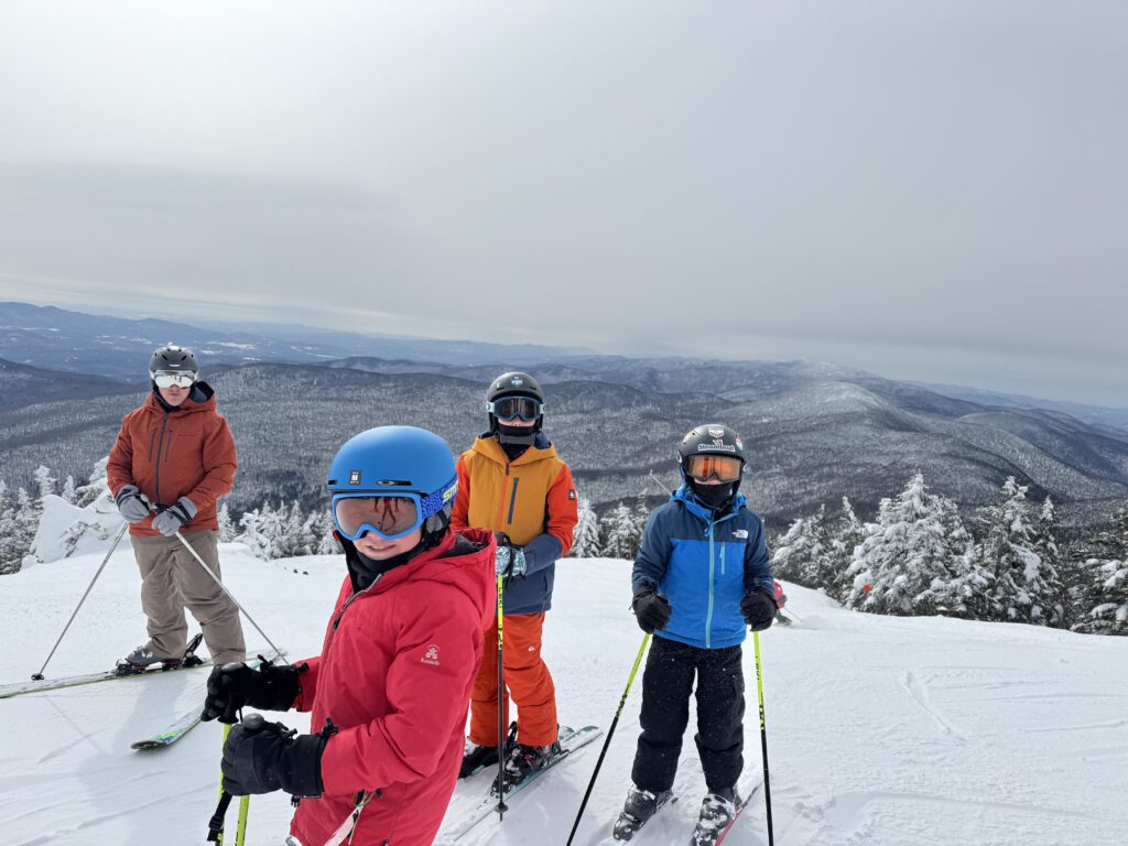 image of kids with skies on at top of stowe mountain with view of vista